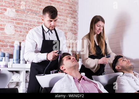 Männer schiefen Köpfen an Waschbecken und entspannend, während Friseure waschen ihre Haare im barbershop Stockfoto