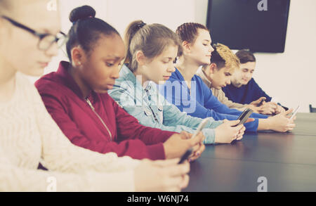 Positive englisch Mitschüler über ihre Smartphones intensiv während der Klassen Stockfoto