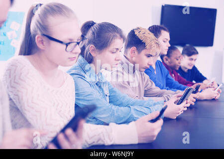 Positive junge männliche und weibliche Studenten spielen mit ihren Smartphones in der Schule Stockfoto