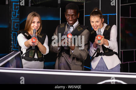 Afrikanische Mann und zwei Erwachsenen kaukasischen Frauen holding Laser Gewehren und auf der Laser tag Zimmer posing Stockfoto