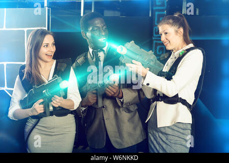 Afrikanischer Mann und zwei hübsche kaukasischen Frauen holding Laser Gewehren und auf der Laser tag Zimmer posing Stockfoto