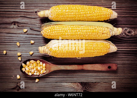 Maiskörner in Holzlöffel neben frischen süßen Bio Hühneraugen auf Holz rustikal Tisch. Gesunde Ernährung Konzept. Stockfoto