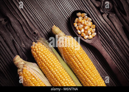 Maiskörner in Holzlöffel neben frischen süßen Bio Hühneraugen auf Holz rustikal Tisch. Gesunde Ernährung Konzept. Stockfoto