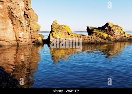 Bild von einigen farbigen Felsen auf ruhigem Wasser in einer Bucht in Dunmore East Village in County Waterford, Irland. Stockfoto