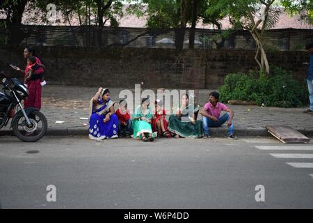 Indische Familie sitzt auf dem Bürgersteig warten auf das Neue Jahre Day Parade in Fort Kochi, Kerala, Indien zu gehen. Stockfoto