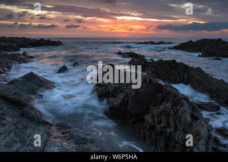 Wellen über die Felsen am Westward Ho! Strand bei Sonnenuntergang in North Devon, England Stockfoto