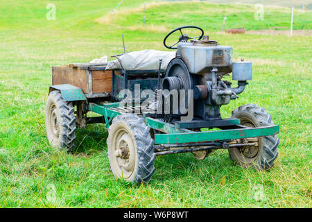 Alter Bauernhof Traktor mit einem hölzernen Sattelanhänger auf eine grüne Wiese Stockfoto