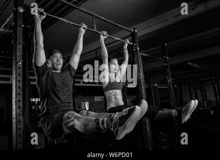 Eine athletische junge Paar ist ein fitness training zusammen und Spaß haben. Starke Mann und Frau tun die Übung l auf der horizontalen Leiste sitzen. Stockfoto