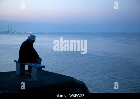 Alte Mann sitzt auf der Bank am Meer Stockfoto