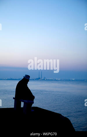 Alte Mann sitzt auf der Bank am Meer Stockfoto