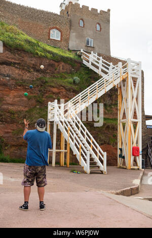 Der Clock Tower Cafe und Bäckerei (Westwand) von Sidmouth Strand gesehen, und Jacobs Leiter Treppe Zugang bietet. Ein jongleur Praktiken Jonglieren an der Promenade. Sidmouth Großbritannien (110) Stockfoto