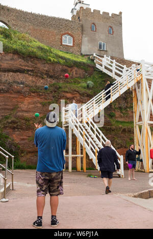 Der Clock Tower Cafe und Bäckerei (Westwand) von Sidmouth Strand gesehen, und Jacobs Leiter Treppe Zugang bietet. Ein jongleur Praktiken Jonglieren an der Promenade. Sidmouth Großbritannien (110) Stockfoto