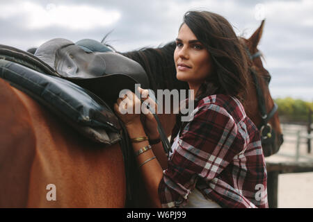 Schöne junge Frau zur Festsetzung einen Sattel auf ihr Pferd. Cowgirl, Pferd für Sie bereit. Stockfoto