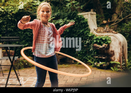 Lächelnd kid Spielen mit einem Hula-Hoop-Reifen in Ihrem Hinterhof. Mädchen Spaß haben eine hoopla Ring um ihre Taille. Stockfoto