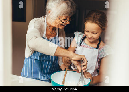 Ältere Frau Lehre ein Kind Teig für Kuchen zu machen. Lächelnde Großmutter und Mädchen mischen Teig in eine Schüssel geben. Stockfoto