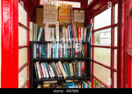 Bücher in den Regalen bilden eine kleine, lokale Bibliothek in einem alten roten Feld/Kiosk/call-Box im Newton Poppleford, Devon. England UK (110) Stockfoto