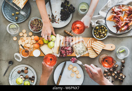 Mitte Sommer Picknick mit Wein und Snacks. Flachbild-lay von Wurst- und Käseplatte, Rose Wein, Nüsse, Oliven und Völker Hände mit Snacks und Wein über Stockfoto