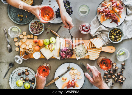 Mitte Sommer Picknick mit Wein und Snacks. Flachbild-lay von Wurst- und Käseplatte, Rose Wein, Nüsse, Oliven und Völker Hände halten Weingläser und ce Stockfoto