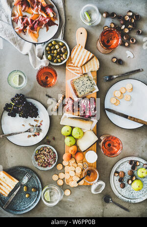 Mitte Sommer Picknick mit Wein und Snacks. Flachbild-lay von Wurst- und Käseplatte, Rose Wein, Nüsse, Oliven und Obst über konkrete Tabelle Hintergrund, t Stockfoto