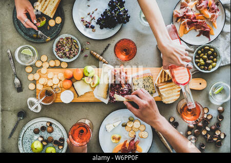 Mitte Sommer Picknick mit Wein und Snacks. Flachbild-lay von Wurst- und Käseplatte, Rose Wein, Nüsse, Oliven und Völker Hände halten Essen und celebrati Stockfoto