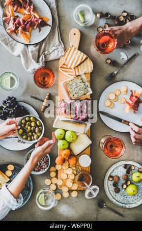 Mitte Sommer Picknick mit Wein und Snacks. Flachbild-lay von Wurst- und Käseplatte, Rose Wein, Nüsse, Oliven und Völker Hände halten Gläser und Essen o Stockfoto