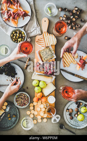 Mitte Sommer Picknick mit Wein und Snacks. Flachbild-lay von Wurst- und Käseplatte, Rose Wein, Nüsse, Oliven und Völker Hände halten Weingläser und Fo Stockfoto