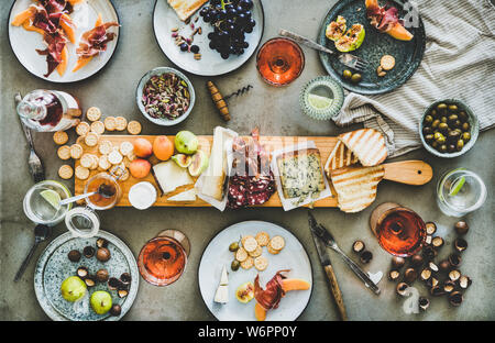 Mitte Sommer Picknick mit Wein und Snacks. Flachbild-lay von Wurst- und Käseplatte, Rose Wein in Flaschen und Gläser, Nüsse, Oliven und Obst über concre Stockfoto