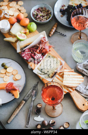 Mitte Sommer Picknick mit Wein und Snacks. Wurstwaren und Käse, Rose Wein, Nüsse, Oliven und Obst über konkrete Tabelle Hintergrund. Familie oder Fr Stockfoto