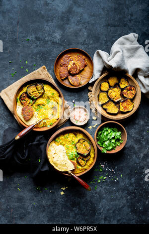 Bengali Khichdi - Linsen, Hirse Suppe - eine Glutenfreie vegane Mahlzeit serviert mit sautierten Aubergine, Mohn Krapfen, und papadum. Stockfoto