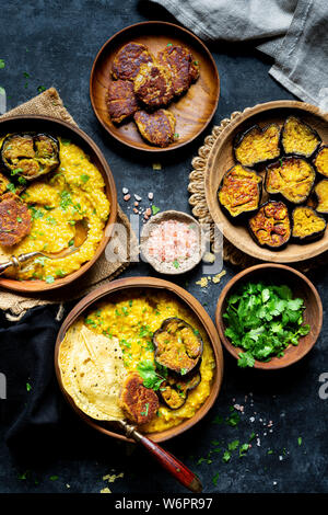 Bengali Khichdi - Linsen, Hirse Suppe - eine Glutenfreie vegane Mahlzeit serviert mit sautierten Aubergine, Mohn Krapfen, und papadum. Stockfoto