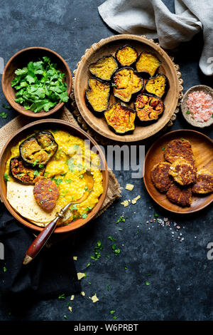 Bengali Khichdi - Linsen, Hirse Suppe - eine Glutenfreie vegane Mahlzeit serviert mit sautierten Aubergine, Mohn Krapfen, und papadum. Stockfoto