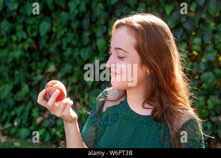 Isolierte junge Frau mit einem Pfirsich ihre Hand. Eine Person, die auf den natürlichen grünen Hintergrund. Stockfoto