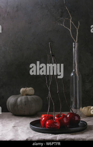 Rot Karamell Apfel süße Herbst Dessert mit Niederlassungen und dekorative Kürbisse in schwarze Keramikplatte auf Leinen Tischdecke mit grauen Mauer bei Bac serviert. Stockfoto