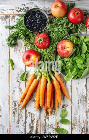 Auswahl an frischem Obst, Gemüse und Beeren Karotten, Spinat, Tomaten, rote Äpfel, Heidelbeeren über weiß Plank Holz- Hintergrund. Flach, Raum Stockfoto