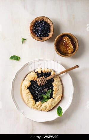 Home backen Sommer berry Keks Kuchen mit Blaubeeren, in der Platte serviert mit Schüssel von Blueberry und Honig mit weißem Marmor Hintergrund. Flach, Raum Stockfoto