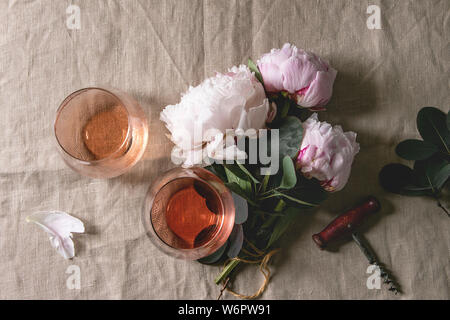 Zwei Gläser verschiedener Rose Wein stehend auf grau Leinen Tischdecke mit rosa Pfingstrosen Blumen. Romantische Grusskarten. Flach, Raum Stockfoto