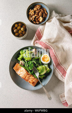 Ketogenic niedrige carb Diät essen gegrillter Lachs, Avocado, Brokkoli, grünen Bohnen und weich gekochte Eier in Keramik Schüssel mit Oliven und Nüssen über Graues serviert. Stockfoto