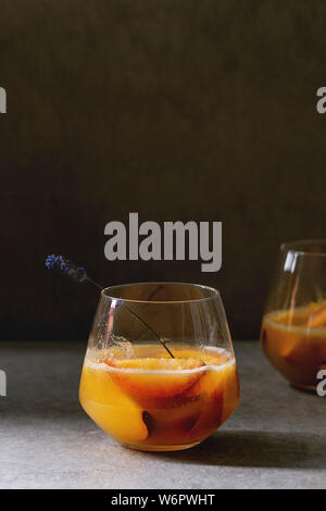 Pfirsich kalte Limonade oder Bellini Cocktail mit Lavendelblüten diente in zwei Gläser auf dunklen Textur Tabelle. Hausgemachte Sommer trinken. Platz kopieren Stockfoto