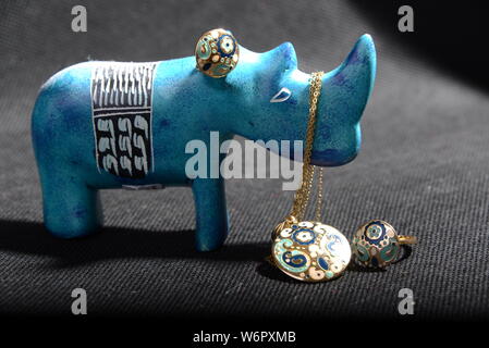 Schmuck auf die kleine blaue rhino Statue halten Sie den Schmuck Halter blau Halskette Gold Ringe Blau und Gold Ringe mit grauem Hintergrund hübsches Tier Stockfoto