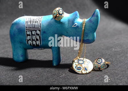 Schmuck auf die kleine blaue rhino Statue halten Sie den Schmuck Halter blau Halskette Gold Ringe Blau und Gold Ringe mit grauem Hintergrund hübsches Tier Stockfoto