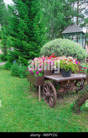 Altes holz vintage Trolley mit Blumenkübel und Kästen mit bunten Blumen und Petunien Geranien im Garten an einem sonnigen Sommertag, vertikal gedreht. Stockfoto
