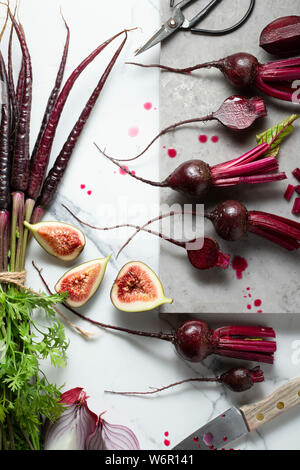 Baby, rote Beete, Karotten Lila, Lila Zwiebeln und Feigen, in Scheiben geschnitten, und auf einem Marmor Fliesen Oberfläche bereit. Ein Messer, Schere und einem Marmorbad board i Stockfoto