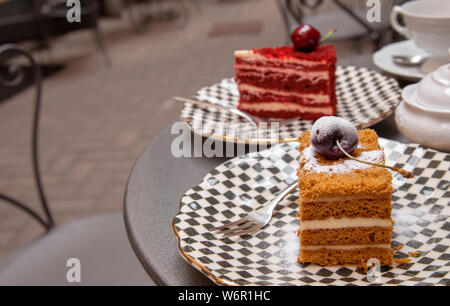 Und eine Kirsche auf der Oberseite - zwei Stücke aus verschiedenen Kuchen auf einem Tisch in einem Patio Cafe gesetzt Stockfoto