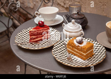 Und eine Kirsche auf der Oberseite - zwei Stücke aus verschiedenen Kuchen auf einem Tisch in einem Patio Cafe gesetzt Stockfoto