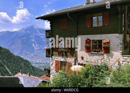 Chalet aus Stein und Holz mit roten Fensterläden aus Holz und Blumen auf der Windows gegen die Berge in den Schweizer Alpen im Dorf Condemines Stockfoto
