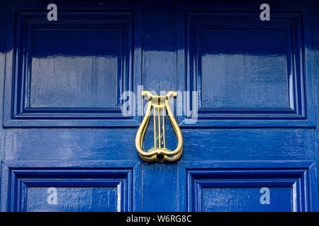 Golden Türklopfer in Form eines irischen Harfe auf einem dunkelblauen Holz- Vordertür Stockfoto