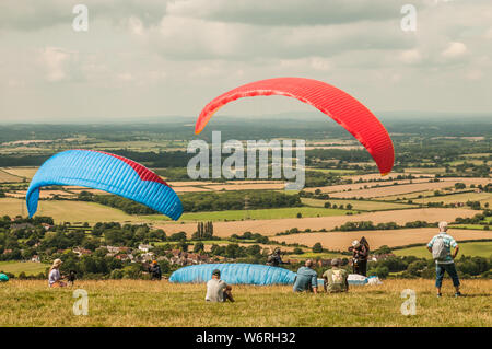 Devils Dyke, Brighton, East Sussex, Großbritannien. Aug. 2019. Ein glorreicher Nachmittag mit einer nördlichen Brise sieht Gleitschirmflieger und Zuschauer am beliebten Veranstaltungsort in den South Downs nördlich von Brighton. Stockfoto