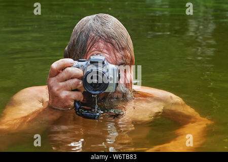 Reifen bärtiger Mann mit wasserdichte Kamera in den Händen macht Fotos beim Schwimmen im Fluss. Stockfoto