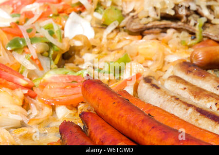 Hot Dogs und Würstchen mit Zwiebeln, Jalapenos, und mehrere Sorten von Paprika und Tomaten Grillen auf einem Outdoor Anbieter Grill. Close Up. Stockfoto