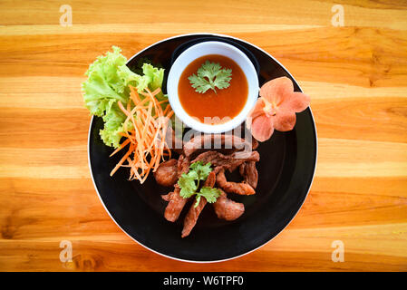 Frittierte Rind- oder Schweinefleisch mit Soße und frisches Gemüse auf dem Teller in den hölzernen Tisch anzeigen/Thai Fried Sonne getrocknetem Rindfleisch asiatisch Essen Stockfoto